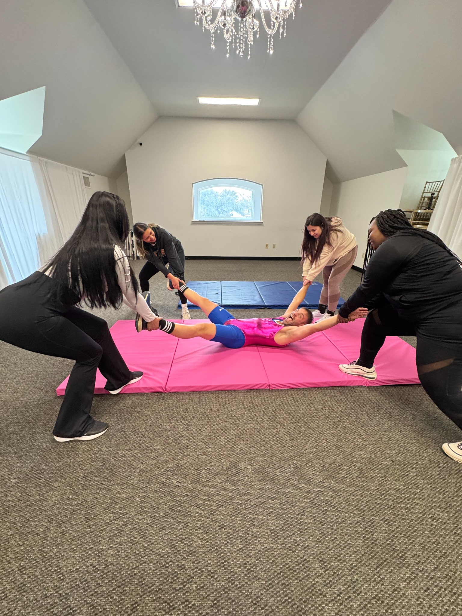 Four women playfully pull Jesse by his arms and legs on a pink mat