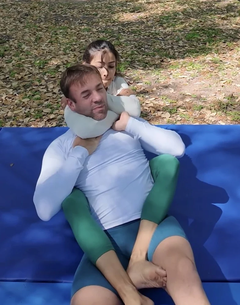 A woman practicing a rear choke during an outdoor class